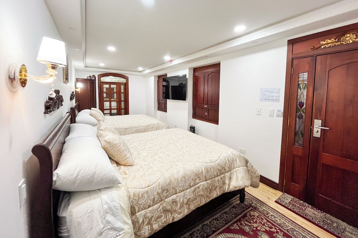 A hotel room with two beds, a wooden wardrobe, a television, and a door with a decorative glass panel.