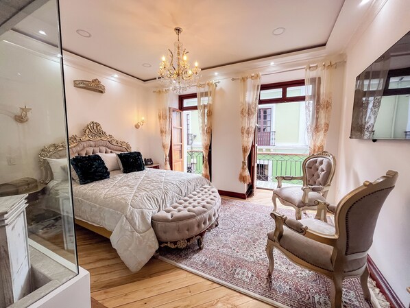 Ein Schlafzimmer mit einem großen Bett, einer Chandelüster, einer Sitzecke mit einem Sessel und Blick auf den Balkon.