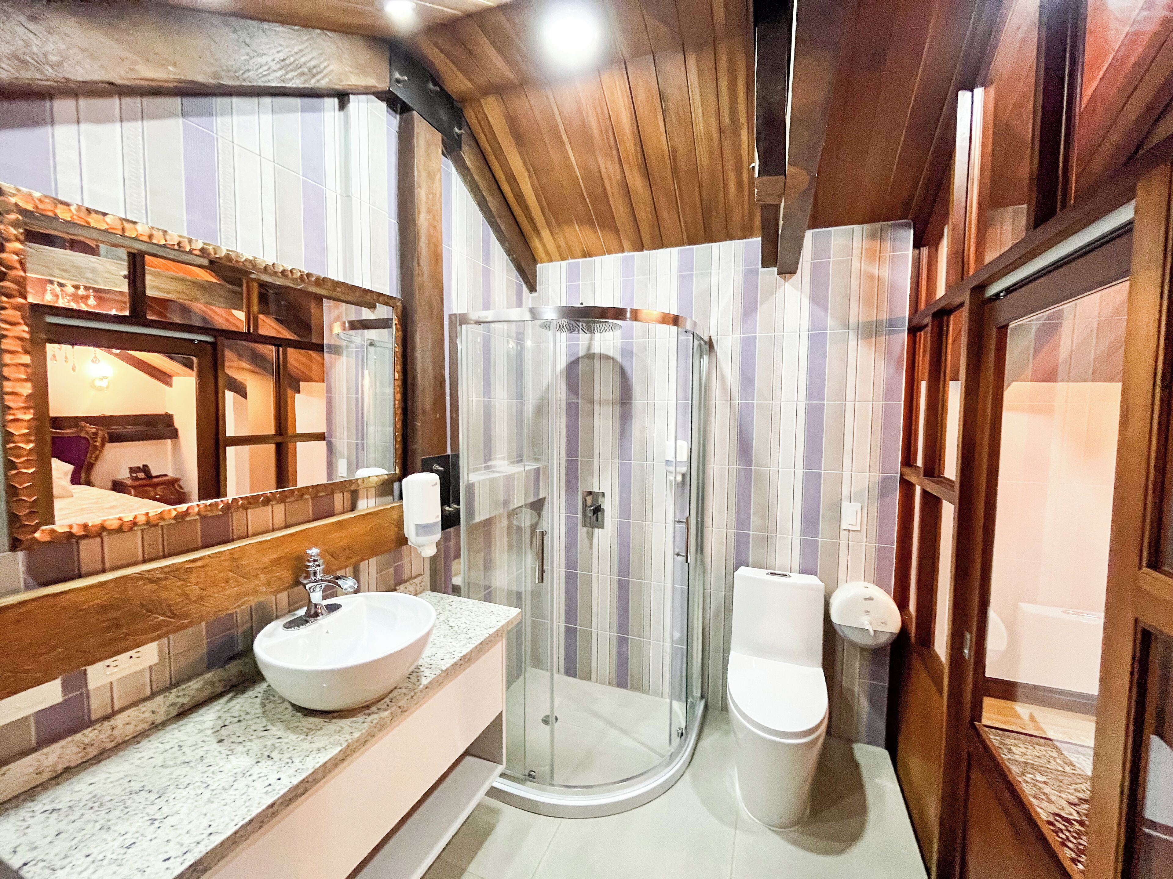 Bagno con soffitto in legno, cabina doccia in vetro, lavabo in marmo e water.