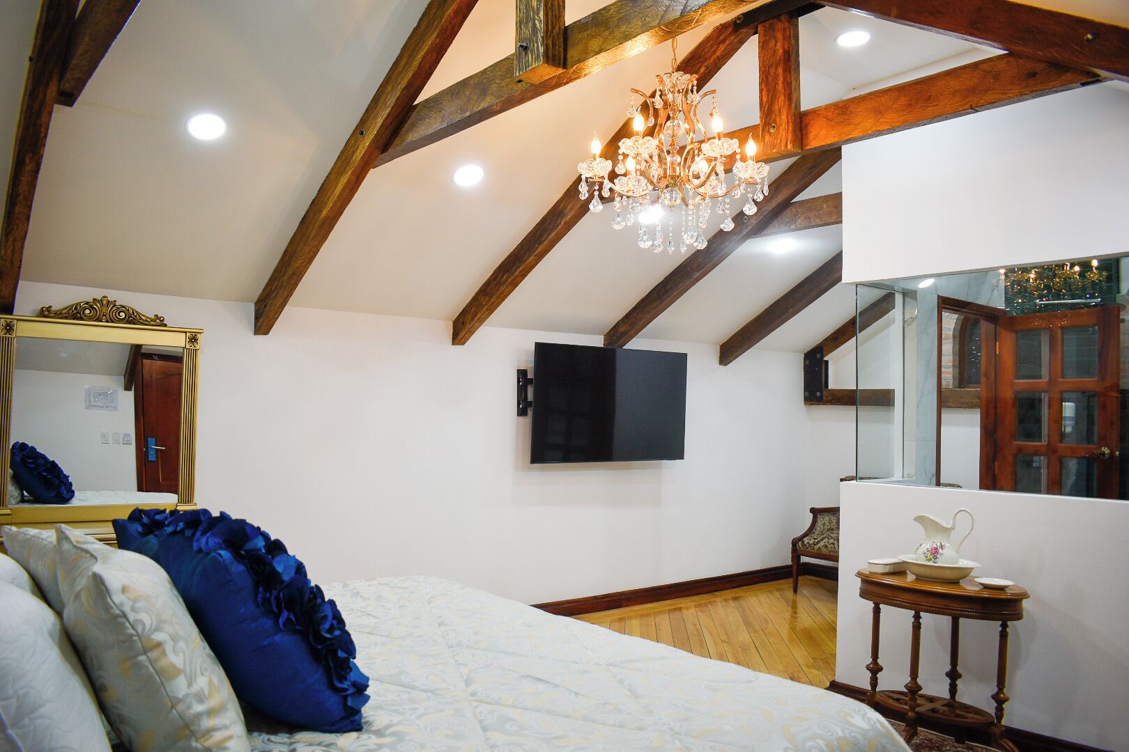 A bedroom with a bed, a chandelier, a television, and a mirror.
