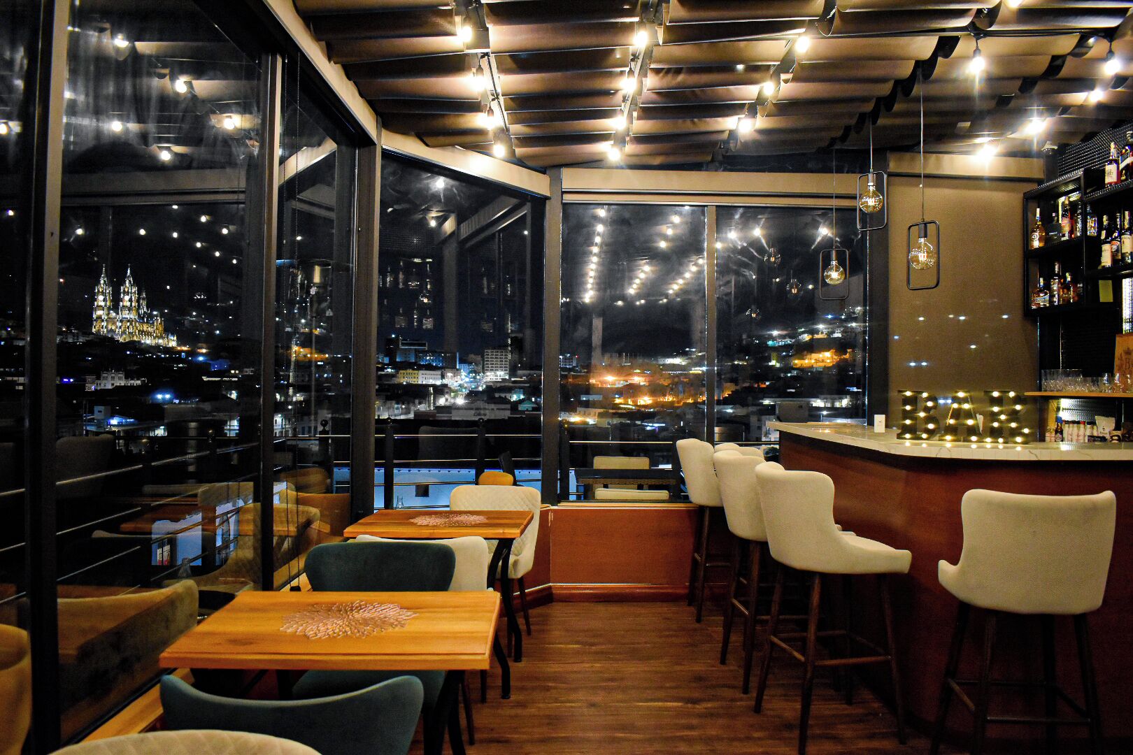 A bar area with a city view, wooden tables, and bar stools.
