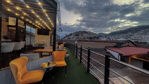 An outdoor seating area with chairs and tables, a railing, and a view of a cityscape with buildings and a hill in the background. - Hotel & Rooftop King Experience by David (Quito)