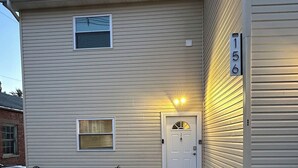 Un bâtiment à deux étages avec une porte d’entrée, trois plantes en pot et une enseigne portant le numéro « 156 ».