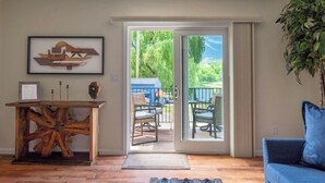 A room with a wooden coffee table, a framed picture on the wall, a blue sofa, and a sliding glass door leading to an outdoor seating area. - Summer on the Creek- Hot Tub • Sauna • Fire Pit • Creek Views (Saugerties)