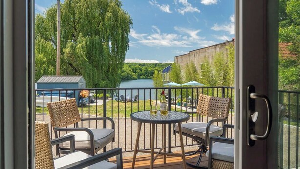 Un balcon avec des fauteuils en osier, une table ronde et une vue sur une rivière et la verdure.
