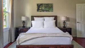 A bedroom with a wooden bed, two bedside tables with lamps, a painting on the wall, and a door. - Summer on the Creek- Hot Tub • Sauna • Fire Pit • Creek Views (Saugerties)