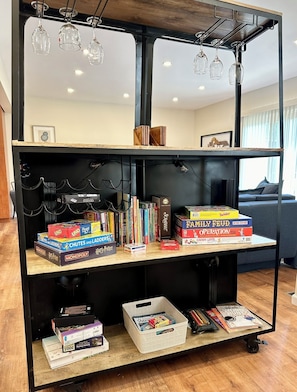 Ein Bücherregal mit verschiedenen Gesellschaftsspielen und Büchern, ein kleiner Tisch mit Schreibwaren und eine Pendelleuchte.