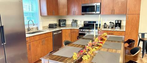 A modern kitchen with wooden cabinets, stainless steel appliances, a dining table with chairs, and a decorative centerpiece.