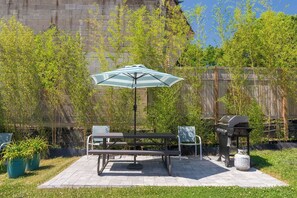 Eine Terrasse mit Tisch, Stühlen, Sonnenschirm und Grill.
