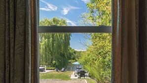 Une vue à travers une fenêtre avec des rideaux, dévoilant un espace extérieur comprenant une pelouse, une table, des chaises et un chemin.