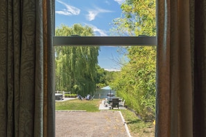 Blick durch ein Fenster mit Vorhängen, der einen Außenbereich mit Rasen, einem Tisch, Stühlen und einem Weg zeigt.