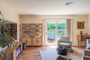 Un salon avec un canapé, un meuble en bois, une plante et une vue sur la verdure à travers une porte vitrée.