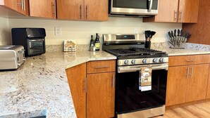 Una cocina con armarios de madera, un microondas de acero inoxidable, un tostador, una estufa a gas y un horno de acero inoxidable.