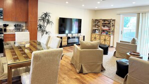 Una sala moderna con una mesa de comedor de madera, sillones color beige, un televisor de pantalla plana y una estantería.