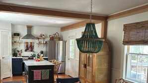A spacious kitchen with a central island, wooden chairs, a dining table, and a hanging green chandelier.