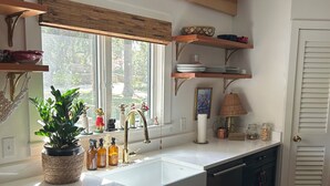 A kitchen with a large window, wooden beams, dark cabinets, and a white countertop.