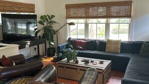 A spacious living room with a large flat-screen TV, leather sofas, a coffee table, and a potted plant.