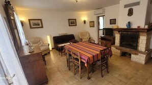 A dining area with a long table, chairs, a fireplace, and a television.