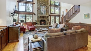 Un salón amplio con chimenea de piedra, ventanas grandes y una escalera de madera.