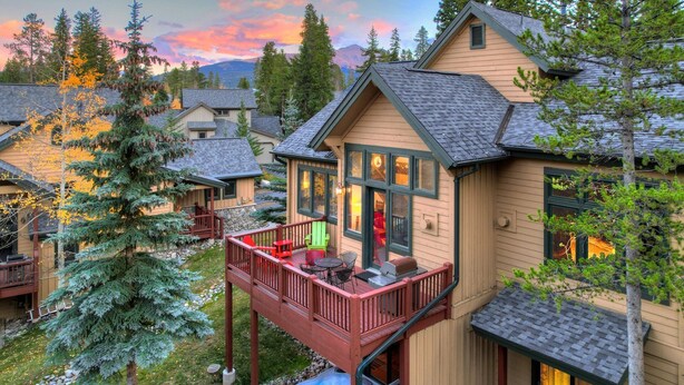 A two-story cabin with a balcony, a hot tub, and a deck with outdoor seating.