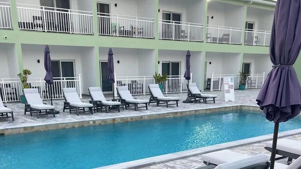 A poolside area with lounge chairs and umbrellas, a pool, and a building with balconies in the background. - Ocean Breeze Resort 1 Bedroom Suite - Boutique Hotel with Pool, Restaurant & Gym (North Caicos)