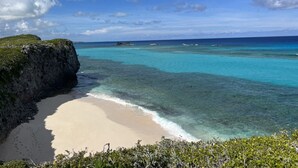 A beach with clear turquoise water, a sandy shore, and a rocky cliff. - Ocean Breeze Resort 1 Bedroom Suite - Boutique Hotel with Pool, Restaurant & Gym (North Caicos)