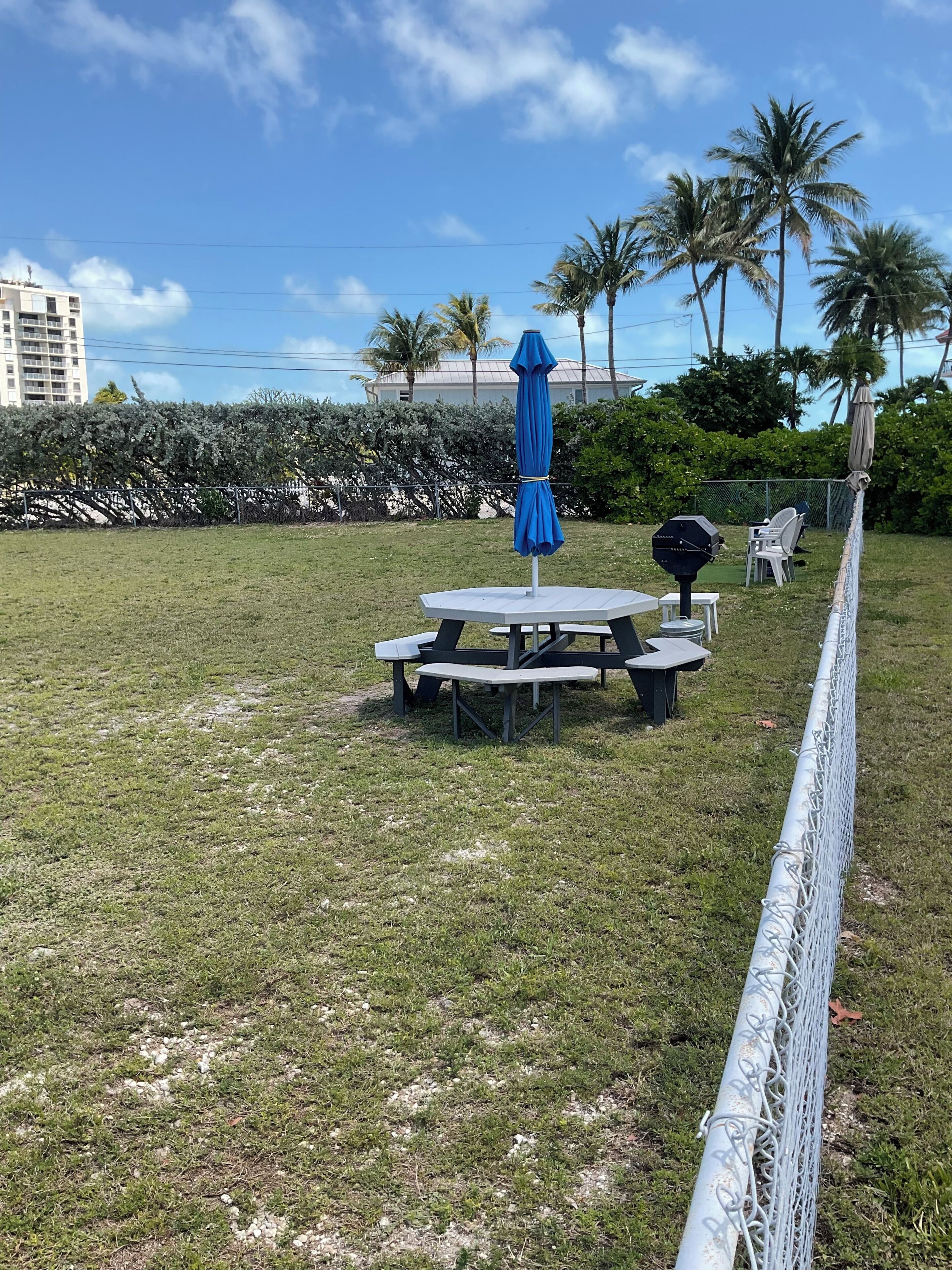 An outdoor seating area with a table and chairs, a blue umbrella, and a grill.