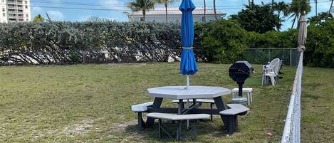 An outdoor seating area with a table and chairs, a blue umbrella, and a grill.