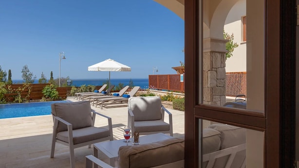 Un espace aménagé au bord de la piscine, avec des chaises longues, une table et une vue sur l’océan.