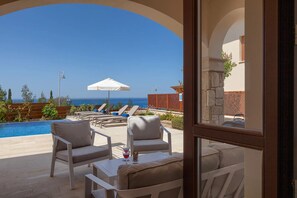 A poolside area with lounge chairs, a table, and a view of the ocean. - Unmatched Luxury: Stunning Views & Elegance at Paphos Villa 1470. (Paphos)