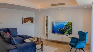 A modern living room with a sofa, a blue armchair, a TV on a wall-mounted stand, and a decorative vase. - Luxurious Villa Living at Grand Poseidon, Paphos Villa 1471 (Paphos)