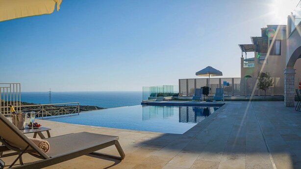 A rooftop infinity pool with a clear view of the ocean, lounge chairs, and a glass-enclosed cabana. - Luxurious Villa Living at Grand Poseidon, Paphos Villa 1471 (Paphos)