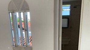 A room with a patterned floor, a small window with bars, and a doorway leading to a bathroom with a sink and tiled walls. - Studio (unfurnished) Monthly (Neópolis Natal)