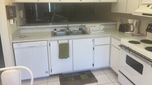 Une cuisine compacte avec des meubles blancs, un lave-vaisselle, une cuisinière et une machine à café.