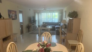Un coin repas avec une table dressée pour quatre personnes, entourée de chaises, d’un vase de fleurs et offrant une vue sur le salon.