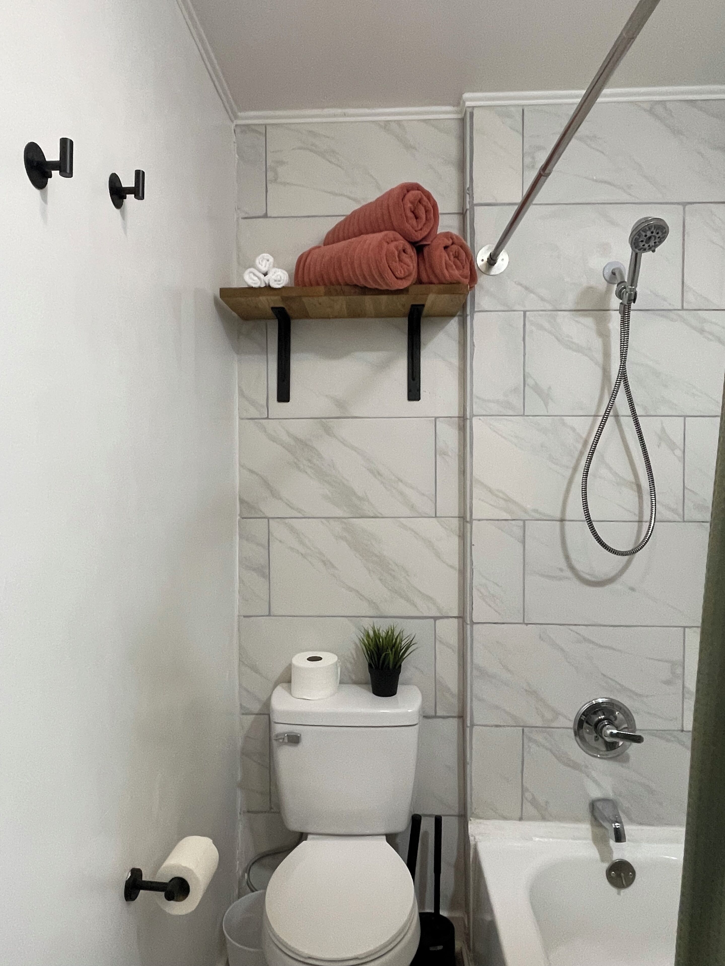 A bathroom with a toilet, a shower, a sink, a towel rack with towels, and a small potted plant.