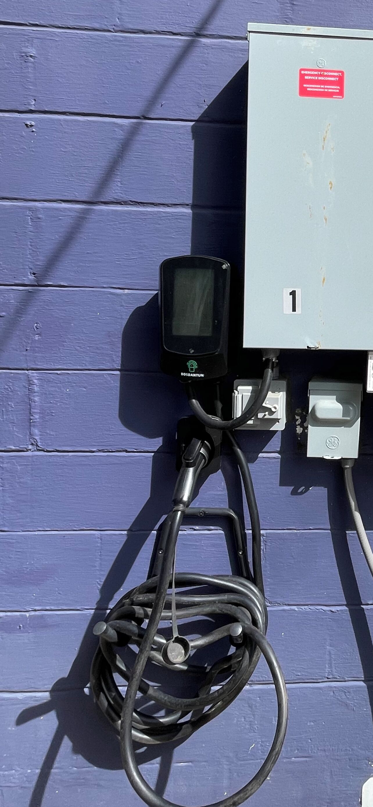 A utility meter with a digital display, connected to a power box marked with the number '1' and an emergency disconnect sticker.