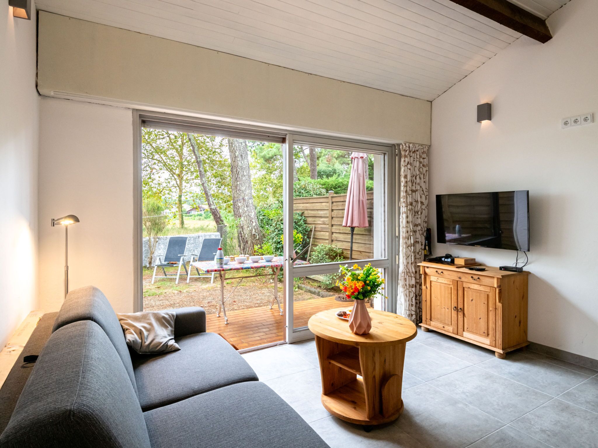 A modern living room with a sofa, a wooden cabinet, a TV, and a sliding glass door leading to an outdoor area with a table and chairs.