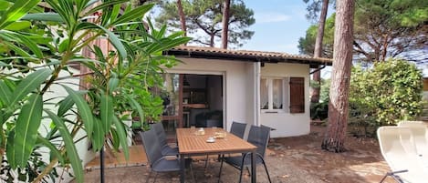 Une petite maison avec un toit en tuiles, une table de patio avec des chaises et de la verdure tout autour.