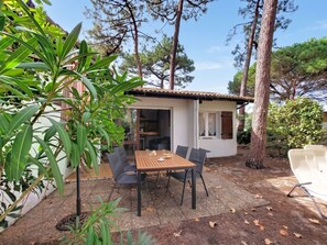 Une petite maison avec un toit en tuiles, une table de patio avec des chaises et de la verdure tout autour.