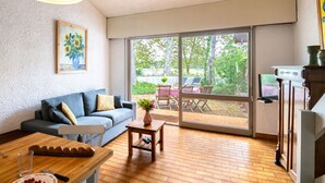 Un salón con sofá, una mesa de centro y una mesa de comedor. Hay un cuadro en la pared y una ventana con vistas al exterior.