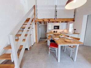 A modern kitchen with white cabinets, a wooden staircase, and a dining area with a table set for four. - Hameau du courant by Interhome (Mimizan)
