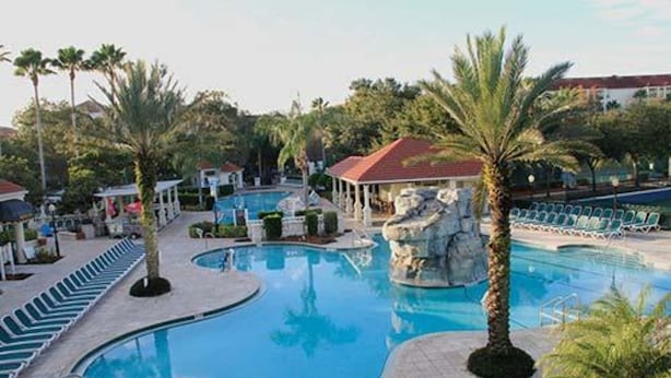 A pool area with lounge chairs, palm trees, and a building with a red roof. - Star Island Resort and Club, just 4 miles from the entrance to Walt Disney World (Kissimmee)