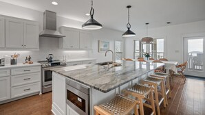 A modern kitchen with white cabinets, a large island, stainless steel appliances, and hanging pendant lights. - Waterfront Fairhope Home / Private Pier, Bayfront Views, Screened in Porch (Fairhope)