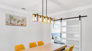 Un comedor con una mesa de madera y sillas amarillas, una lámpara colgante y un cuadro con jarrones en la pared.