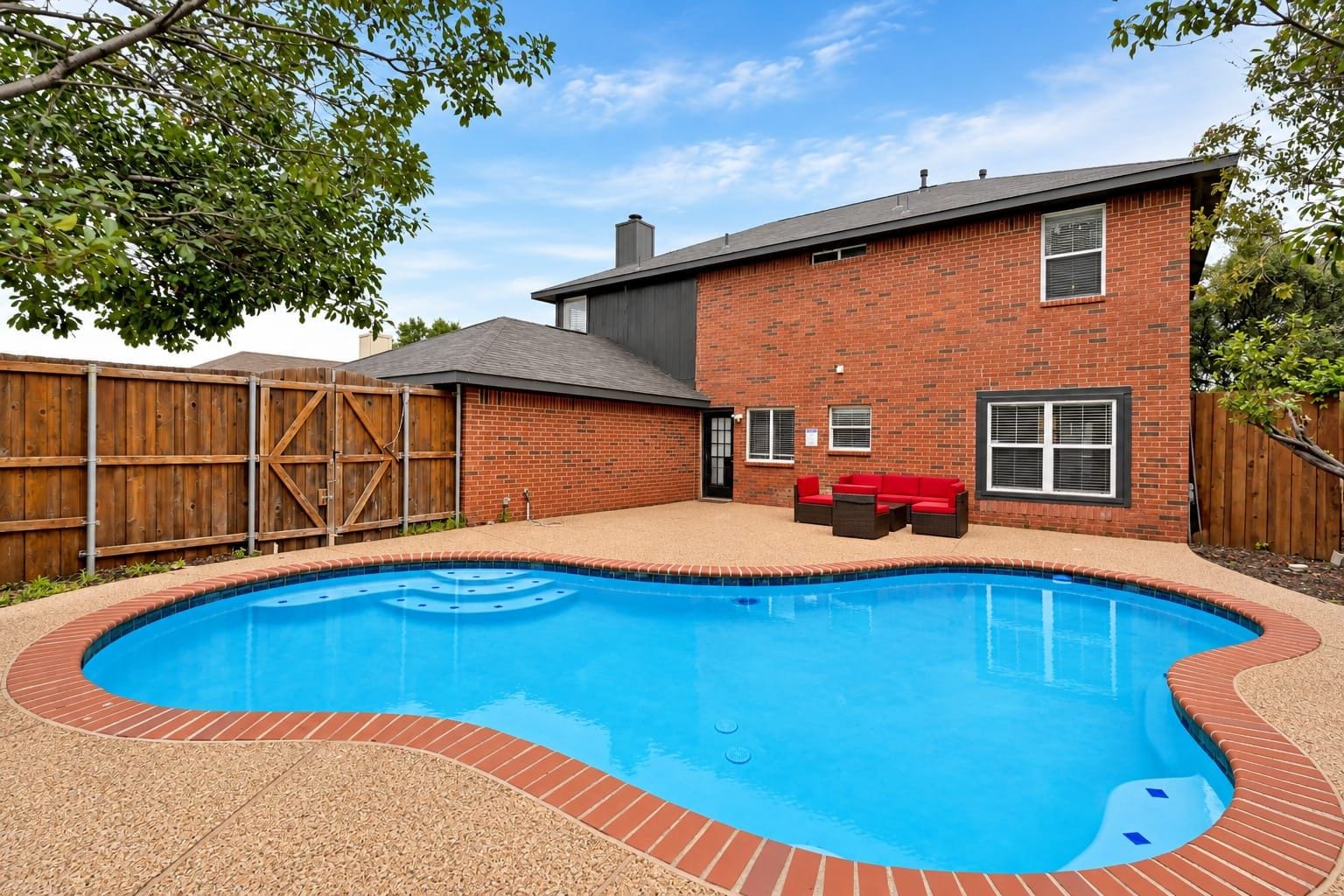 Un patio trasero con piscina, una casa de ladrillo y una valla de madera.