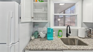 Une cuisine dotée d’un plan de travail en granit, d’un évier, d’une fenêtre et d’un meuble contenant de la vaisselle.