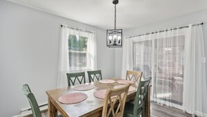 Un coin repas avec une table en bois, des chaises vertes et des rideaux blancs.