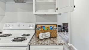 Une cuisine avec des meubles blancs, un fourneau et un panneau d’accueil posé sur le plan de travail.