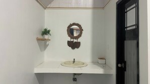 Un baño con un tocador blanco, un espejo con marco decorativo, una planta en maceta sobre una estantería y una puerta negra.
